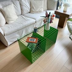 a living room with a white couch and green table in front of the sofa is filled with books