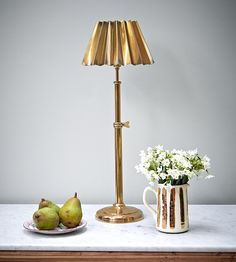 a table with two pears and a gold lamp on it next to a bowl of flowers