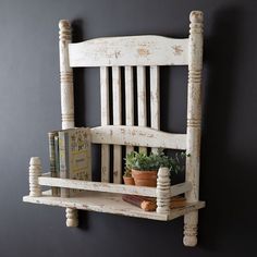 an old white wooden chair with books and plants on the shelf next to it, against a dark gray wall