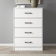 a white chest of drawers with black handles in a room next to a gray wall