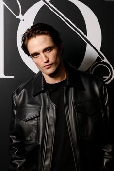 a man wearing a black leather jacket standing in front of a wall