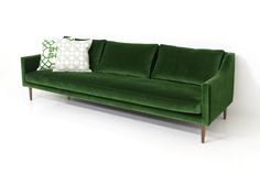 a green velvet couch with two pillows on it's back and one pillow on the arm