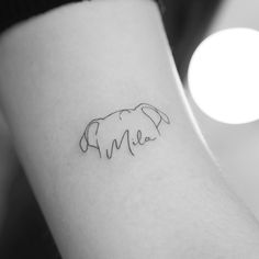 a small elephant tattoo on the left inner arm and shoulder, with an inscription in cursive font