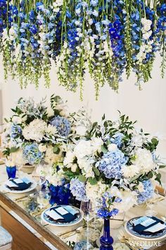 blue and white centerpieces with greenery hanging from the ceiling at a wedding reception