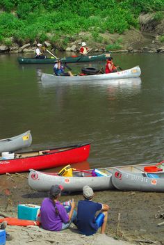 several canoes are lined up on the shore as people sit in their kayaks