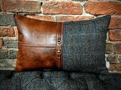 a brown leather and tweed pillow sitting on top of a black couch next to a brick wall