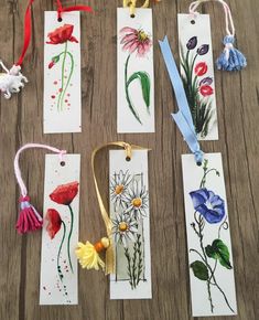 four bookmarks with flowers and tassels hanging from them on a wooden table