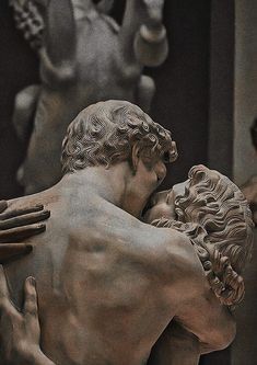 a statue of two men embracing each other in front of some statues with hands on their backs