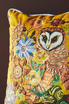 an owl is sitting on top of a yellow pillow with flowers and leaves around it