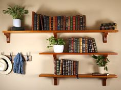 three wooden shelves with books, hats and plants on them against a wall filled with books