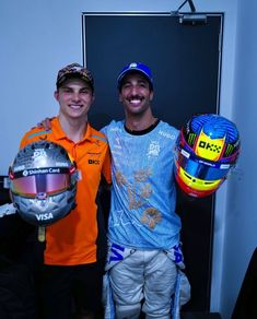 two men standing next to each other holding helmets