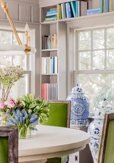 a dining room table with green chairs and vases on the table next to it