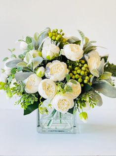 a vase filled with white flowers and greenery