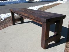 a wooden bench sitting on the side of a road next to snow covered ground and trees