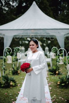 a woman standing in front of a white tent holding a bouquet of red roses