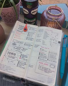 an open planner book sitting on top of a wooden table next to potted plants