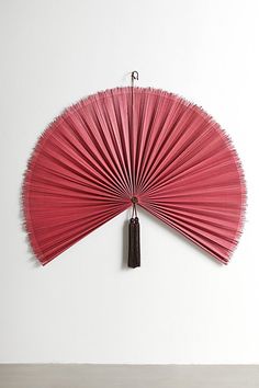 a red fan hanging on the wall in front of a white wall with a black tassel