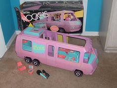 a pink toy bus next to a cardboard box with pictures on it and other toys