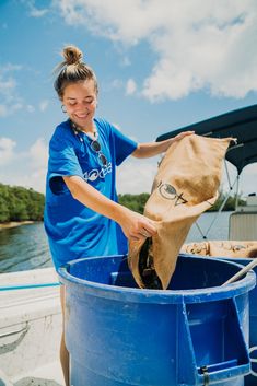 a woman in blue shirt holding a bag over a trash can on a small boat