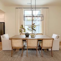 a dining room table with four chairs and a vase on top of it in front of a window