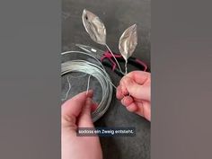 two hands are holding wire with leaves attached to the ends and wires on each side