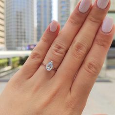 a woman's hand with a diamond ring on top of her finger and buildings in the background