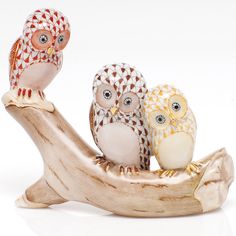 three glass owls sitting on top of a wooden branch with white and red designs around their eyes