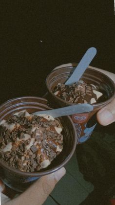 two people holding bowls of food with spoons in them