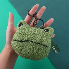 a hand holding a keychain with a green frog on it's face