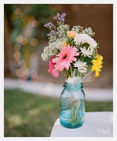 a vase filled with lots of colorful flowers on top of a white tablecloth covered field