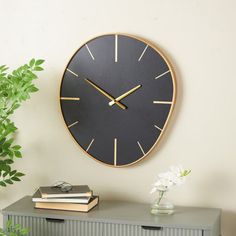 a black and gold clock sitting on top of a wall next to a green plant