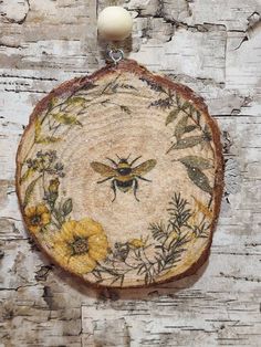 a piece of wood that has been painted with flowers and bees on it, hanging from a chain