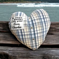 a heart shaped pillow sitting on top of a wooden bench next to the ocean with words written on it