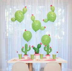 a table topped with lots of green balloons and potted cacti on top of it