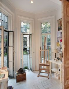 a room with several windows and wooden furniture in the corner, including an easel