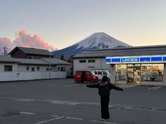 a woman standing in the middle of a parking lot next to a building with a mountain in the background