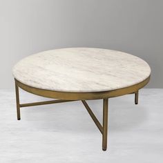 a white marble top coffee table with gold metal legs and an oval shaped base, against a gray background