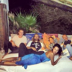 a group of people laying on top of a bed next to each other in front of a potted plant