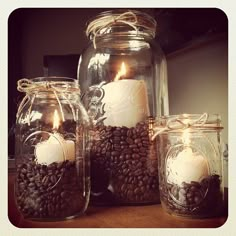 three mason jars filled with coffee beans and lit candles on top of a wooden table