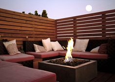 a fire pit sitting on top of a wooden deck next to couches and pillows