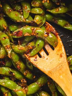 green peppers being cooked with a wooden spatula in a frying pan on the stove