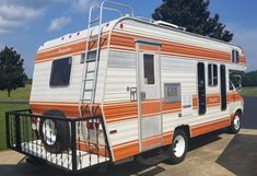 an orange and white camper trailer parked in a parking lot next to a tree