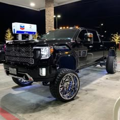 a black truck with chrome rims parked in front of a gas station at night