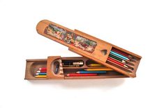 an open wooden box with colored pencils and pens in it on a white surface