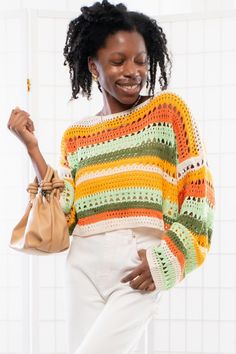 a woman wearing a multicolored sweater and white pants holding a handbag while standing in front of a tiled wall