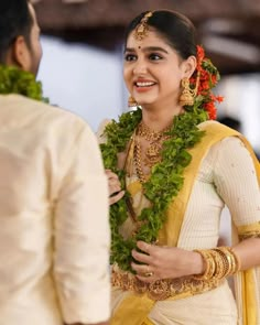 a woman in a yellow and white sari smiles as she stands next to a man