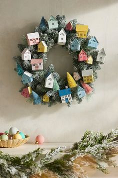 a christmas wreath with houses on it next to other holiday decorations and greenery in front of a white wall