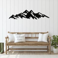 a wooden bench sitting in front of a white wall with mountains on it and welcome home pillows