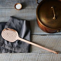 a wooden spatula sitting on top of a cloth next to a pot and spoon