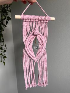 a pink macrame hanging from a wall with a wooden stick in the middle